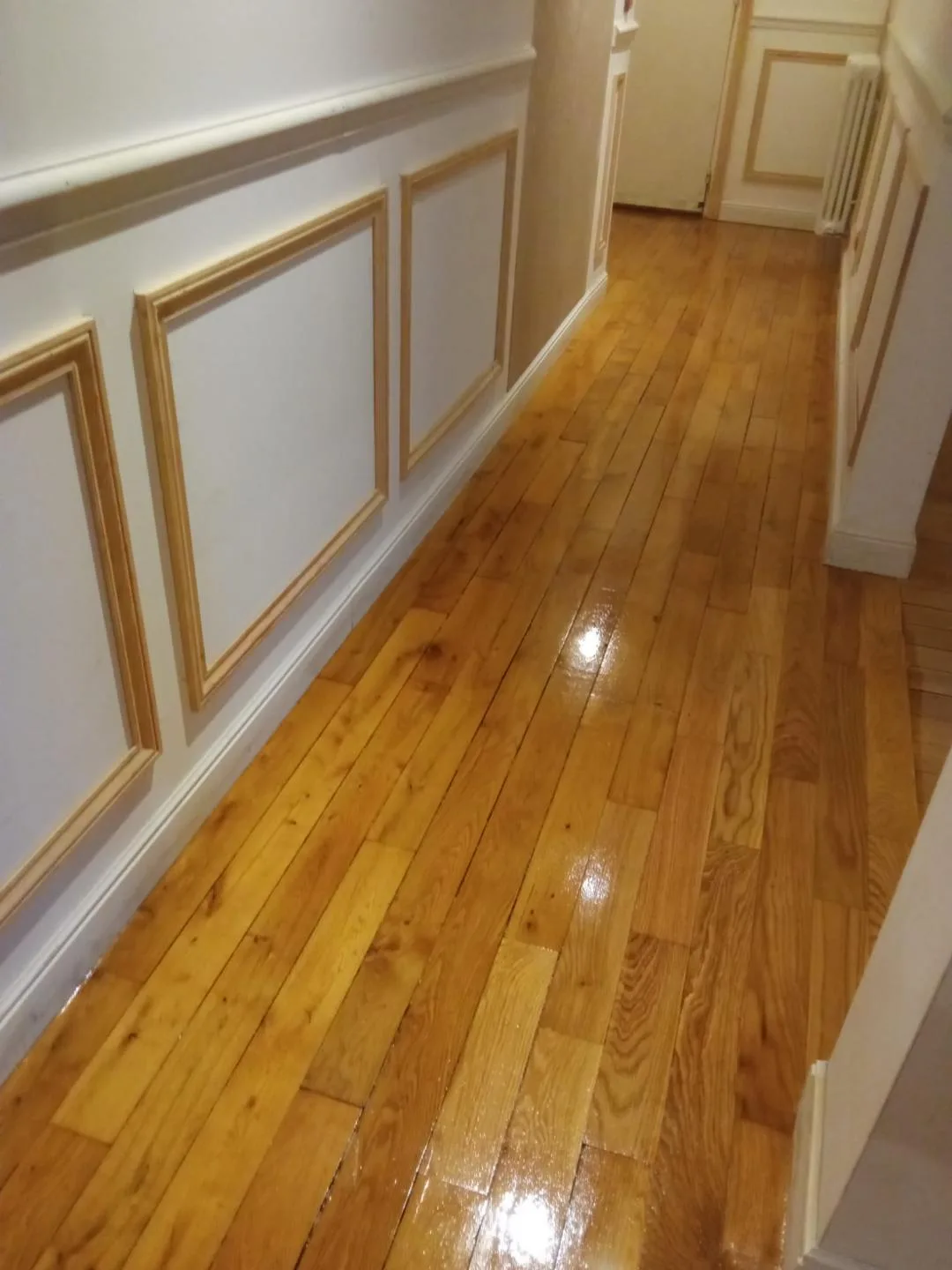Parquet en chêne fraîchement vitrifié dans un couloir à boiseries moulurées